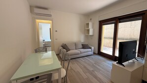 A compact living space with a glass dining table, a sofa, a TV on a cabinet, and a sliding glass door leading to an outdoor area. - Oasi Perugina - maximum comfort in the beating heart of Perugia (Perugia)