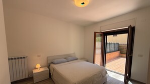 A bedroom with a bed, a nightstand, a lamp, a radiator, and a sliding glass door to a balcony. - Oasi Perugina - maximum comfort in the beating heart of Perugia (Perugia)