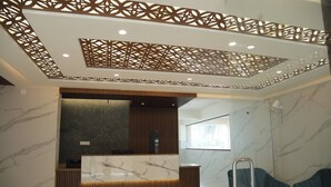 Una moderna área de recepción con un mostrador de mármol, paneles de madera y un techo decorativo.