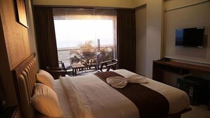 Habitación de hotel con una cama grande, televisor y vista al océano a través de una puerta corredera.
