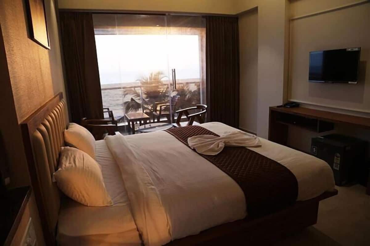 A hotel room with a large bed, a TV, and a view of the ocean through a sliding door.