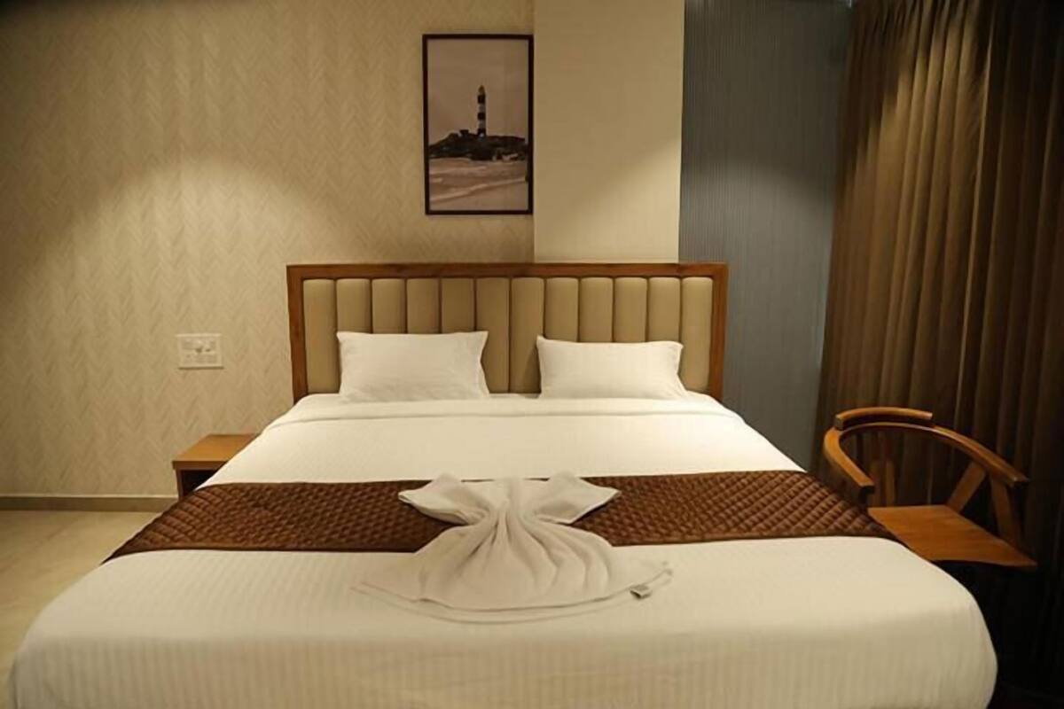 A neatly made bed with a wooden headboard, a folded towel on the bed, a framed picture on the wall, and a wooden chair to the side.