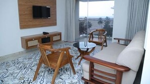 Una sala moderna con un sofá, dos sillones de madera, una mesita redonda, un televisor montado en un panel de madera, y un balcón con vistas.