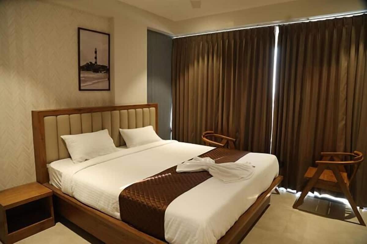 A hotel room with a large bed, two wooden chairs, a small table, and a framed picture on the wall.
