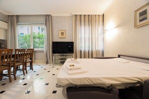 Une chambre dâhĂŽtel avec un lit, une tĂ©lĂ©vision, un bureau avec des chaises et une fenĂȘtre avec des rideaux.