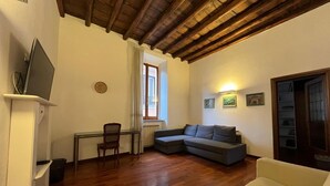 Un salon avec un plafond en bois, un canapé d’angle gris, un fauteuil jaune, une table à manger avec des chaises et un téléviseur posé sur un meuble.