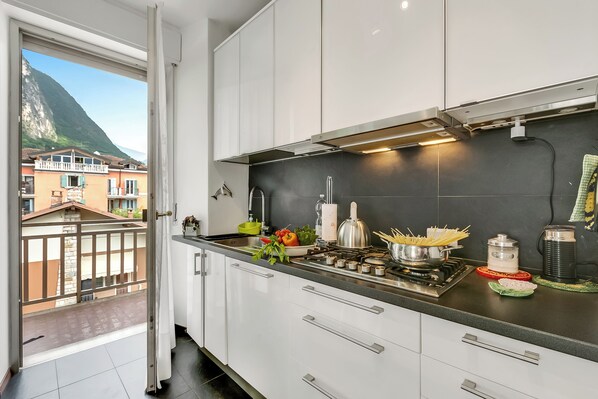 A modern kitchen with white cabinets, a gas stove, and a view of a mountain and buildings through an open door.