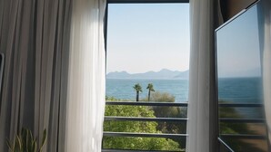 Une chambre avec une grande fenêtre, un lit, une télévision et une bouche d’aération au plafond.
