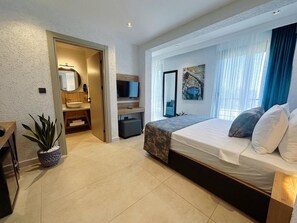 Una habitación de hotel moderna con cama, televisión, baño y un ventanal con cortinas.