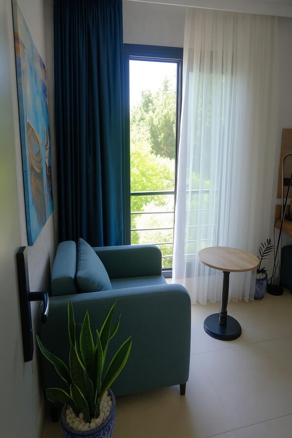 A modern living room with a sofa, a small round table, a potted plant, and a painting on the wall. - Taga Hotel (Bitez)