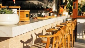 Un espace bar avec des tabourets en bois, un comptoir orné de bouteilles et un panneau néon indiquant « Tago Bar ».