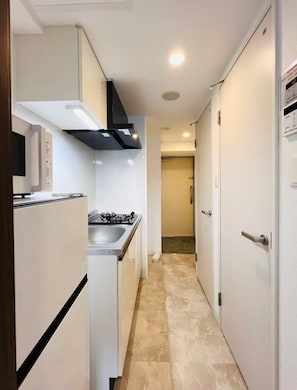 A narrow kitchen with a microwave, stove, and a black range hood. - ARASHI HOTEL TENGACHAYA (Osaka)