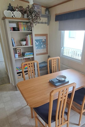 Ruokailutilassa on puinen pöytä ja tuolit, kirjahylly, jossa on kirjoja ja koriste-esineitä, sekä ikkuna, josta on näkymä parvekkeelle.