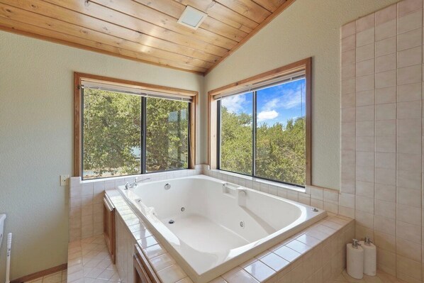 A bathroom with a large bathtub, wooden ceiling, and large windows offering a view of trees. - Lakefront Haven+GameRoom+Canoe with Stunning Views (Somerset)