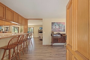 A kitchen with wooden cabinets, a bar area with stools, and a dining table in the background.