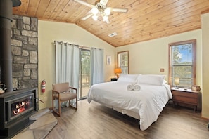 A bedroom with a stone fireplace, a bed, a chair, and a window with blinds.