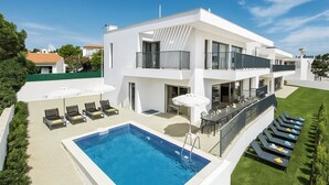 Ein modernes, zweistöckiges Haus mit Swimmingpool, Sitzgelegenheit im Freien und einem gepflegten Rasen.