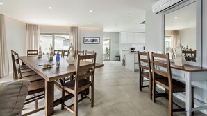 Ein moderner Essbereich mit Holztisch und -stühlen, im Hintergrund eine Küche und eine Wand-Klimaanlage.