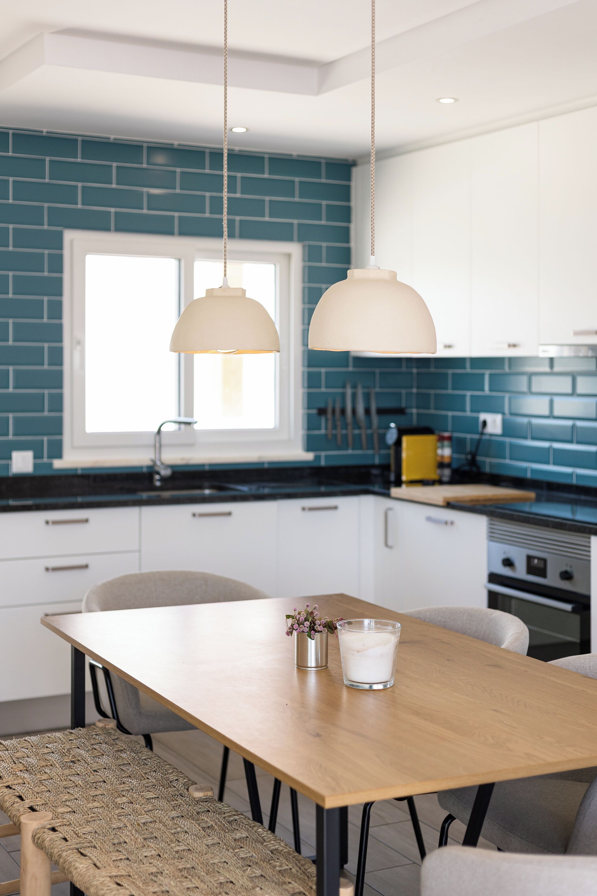 Una cocina moderna con salpicadero azul, armarios blancos y una mesa de comedor de madera con sillas.