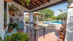 Patio esterno con tavolo in vetro, sedie e piante in vaso.