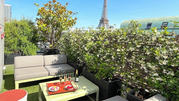 A rooftop terrace with outdoor seating, a bottle of champagne, and a tray with snacks. The Eiffel Tower is visible in the background. - Le Penthouse Faure (Paris)