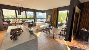 A modern living room with a kitchen area, large windows, and a fireplace. - Le Penthouse Faure (Paris)