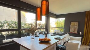 A modern kitchen with a central island, large windows, and a view of greenery outside. - Le Penthouse Faure (Paris)
