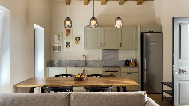 A modern kitchen with a wooden dining table, a built-in oven, and a refrigerator. There are framed pictures on the wall and a bowl of fruit on the table. - Bigtrel Athens (Athens)