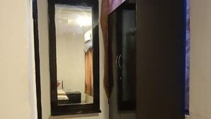 A small, dimly lit room with a single bed, a mirror, a dark cabinet, and a small trash bin. - Hotel Shree Vilas (Nathdwara)