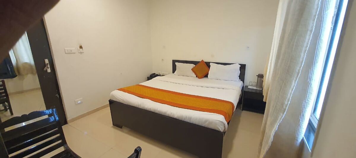 A hotel room with a bed, a nightstand, and a window with curtains.