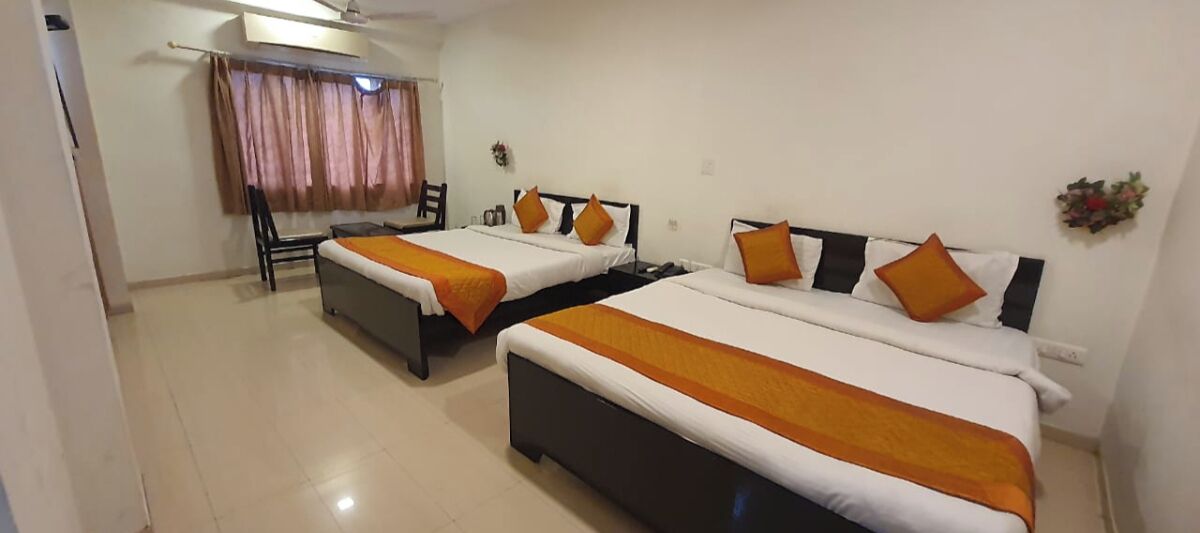 A hotel room with two beds, each with an orange bedspread, a chair, and a window with curtains.