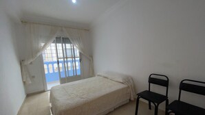 Un dormitorio con cama, dos sillas, un ventanal con cortinas y vistas a una barandilla azul en el exterior.