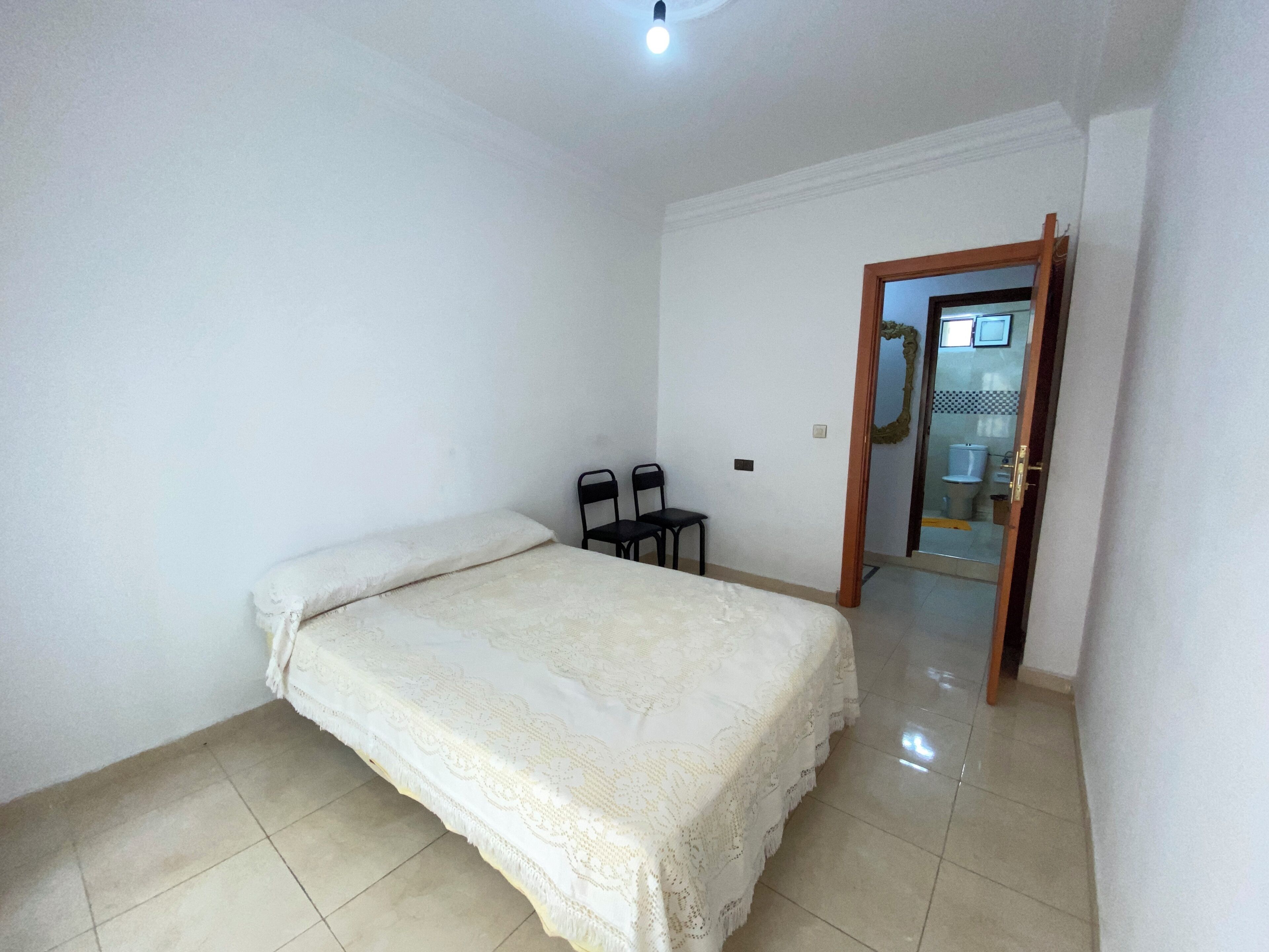 A bedroom with a bed, two chairs, and a door leading to a bathroom.
