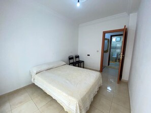 A bedroom with a bed, two chairs, and a door leading to a bathroom. - Comfortable family apartment (Martil)