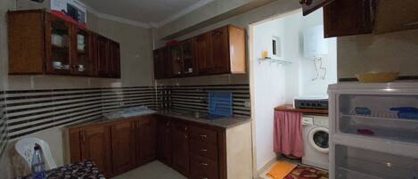 Una cocina compacta con armarios de madera, lavadora y una pequeña mesa con mantel floreado.