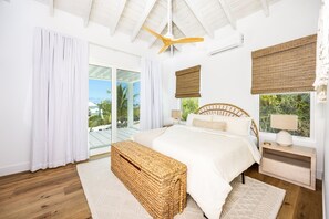 A bedroom with a bed, bedside tables, a ceiling fan, and large windows with curtains.