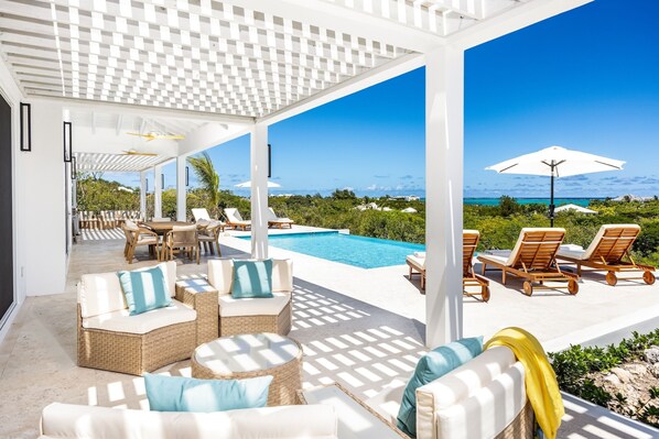 A covered outdoor area with a pool, lounge chairs, and a view of the ocean.