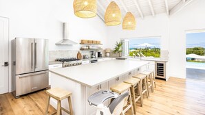 A modern kitchen with a large island, stainless steel appliances, and a view of a mountainous landscape. - AMANERA "peaceful water" NEW Villa with Ocean View - Walk to Beach (The Bight Settlement)