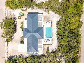 An aerial view of a resort with a central building, a swimming pool, and surrounding greenery.