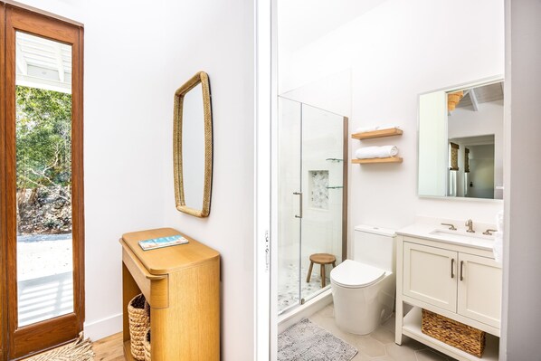 A modern bathroom with a glass shower, white vanity, and a wooden side table.