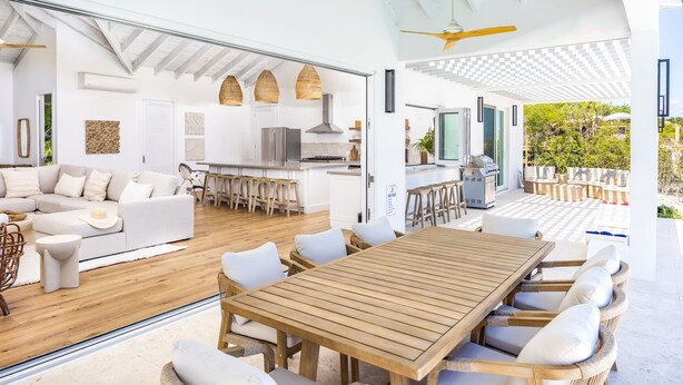 An open-plan living area with a wooden dining table and white furniture, a kitchen with modern appliances, and a view of the outdoors. - AMANERA "peaceful water" NEW Villa with Ocean View - Walk to Beach (The Bight Settlement)