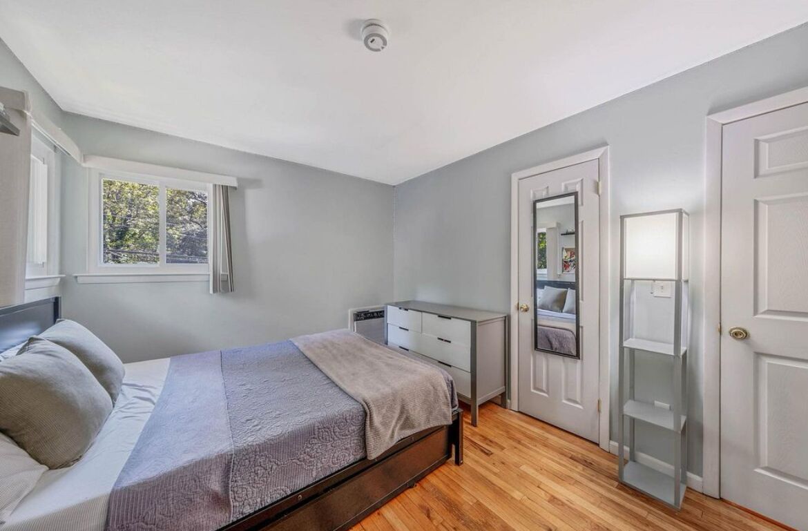 Een slaapkamer met een bed, een ladekast, een spiegel en een deur.