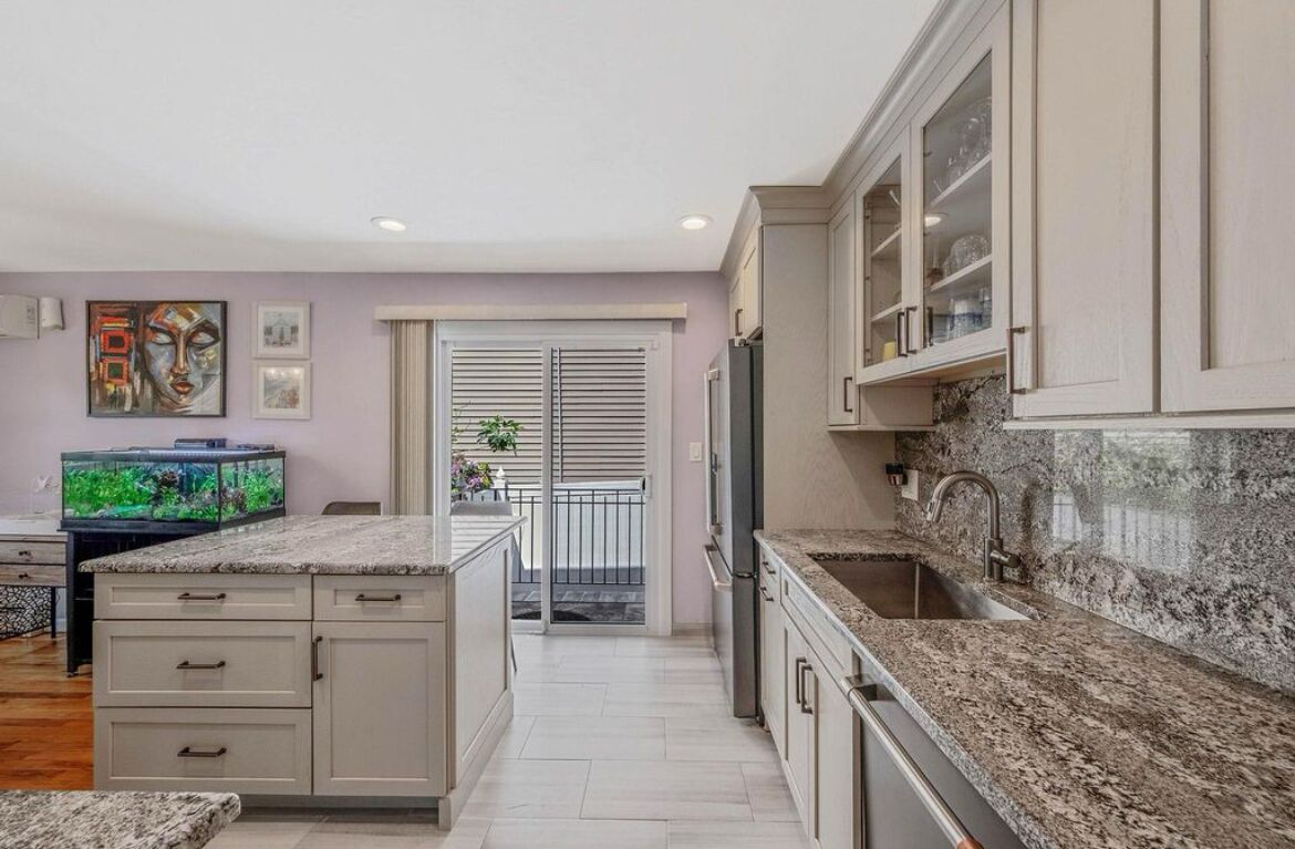 A modern kitchen with granite countertops, a built-in oven, and a stainless steel refrigerator.