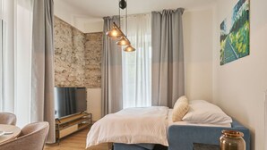 A modern bedroom with a stone wall, a bed with a blue upholstered headboard, a wooden table, and a hanging light fixture.