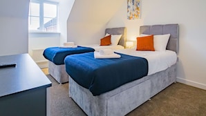Moderni hotellihuone, jossa on kaksi sänkyä, työpöytä ja ikkuna, jossa on sälekaihtimet.