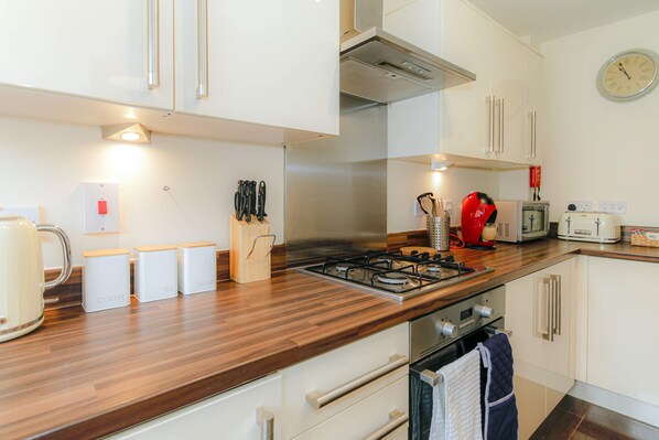 Una cocina moderna con armarios blancos, encimera de madera, cocina a gas, cafetera y microondas.