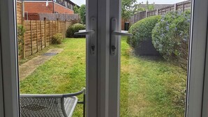 A view through a glass door into a backyard with a wooden fence, a bench, and a hedge. - Kennedy 6 Bedroom 6 Bathrooms House in Hampton (Peterborough)