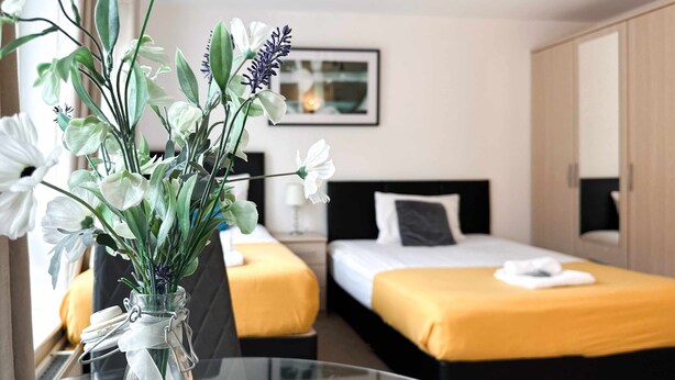 A hotel room with two beds, a glass table with a vase of flowers, and a framed picture on the wall. - Kennedy 6 Bedroom 6 Bathrooms House in Hampton (Peterborough)