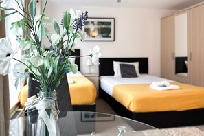 Et hotelværelse med to senge, et sofabord med en vase blomster og et billede i ramme på væggen.