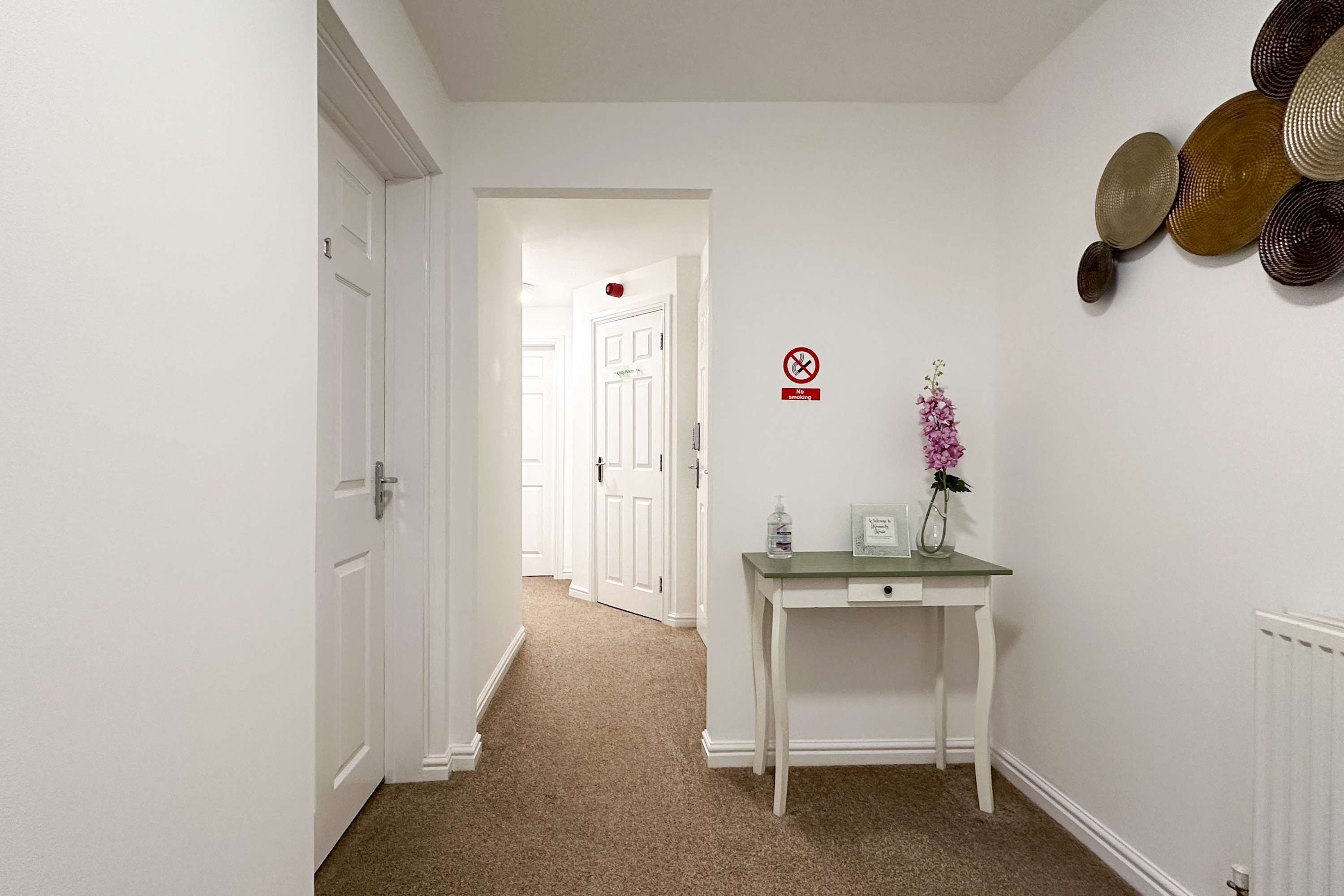 A hallway with white walls, a white door, and a small table with a vase of flowers.